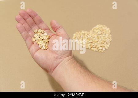 Close-up male caucasian hand holding oats. Shape of heart top view brown background with copy space. Stock Photo