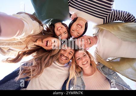 Selfie portrait from below of diverse gen z group friends posing smiling in circle looking at camera Stock Photo