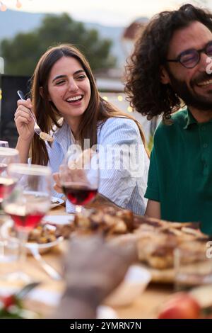 Young adult Caucasian couple smiling sitting at table at friendly summer barbeque outdoors Stock Photo