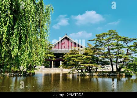 A large red building with a green tree in front of it. The building is surrounded by a pond Stock Photo