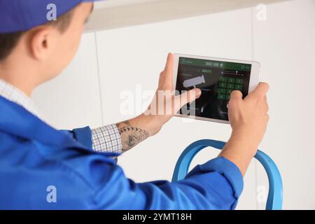 Male worker with tablet installing alarm system in house, closeup Stock Photo