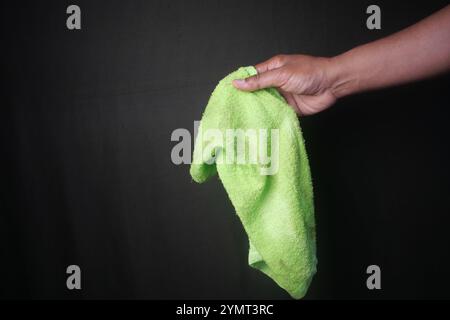 A vibrant green cleaning cloth held in hand stands out against a sleek black background Stock Photo