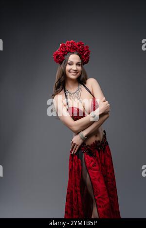 Dancer in vibrant red costume with floral crown posing gracefully in studio Stock Photo