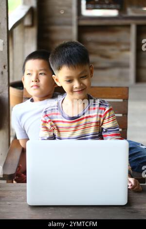 Two boys share a moment over a laptop in a rustic setting, showcasing friendship, curiosity, and the joy of learning through technology. Stock Photo