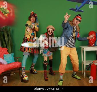 Family of freaks poses and throws a tomato, scrambled eggs and a toy plane at the camera, having fun in the studio on a green background Stock Photo
