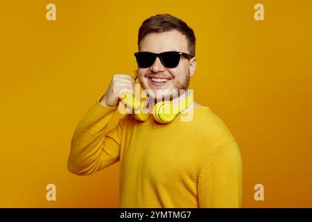 Funny man wearing yellow jumper and sunglasses holding banana like a smartphone near ear and smiling Stock Photo