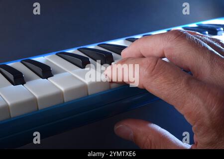 Detail of hand playing blue melodica with blue background and light beam illuminating. Stock Photo