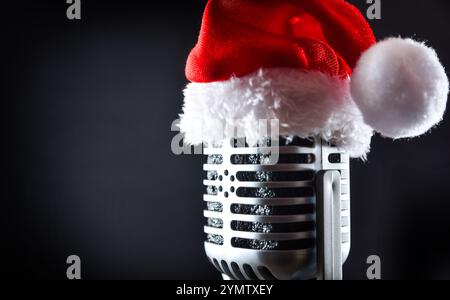 Detail of old microphone with a Santa hat on top, isolated on a black background. Side view. Stock Photo