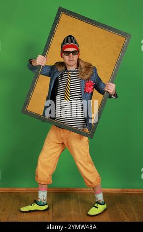 Middle aged male freak holds a picture frame in a studio on a green background Stock Photo