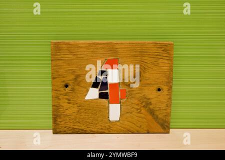 Number 4 house number mosaic made from ceramic tiles and set into a wooden plaque with a green ceramic tile behind it. Stock Photo