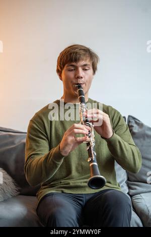 Clarinet player. Man clarinetist playing flute woodwind music instrument sitting on couch at home Stock Photo