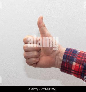 A man's hand clad in a red plaid shirt giving a thumbs up against a clean white background, symbolizing approval or success Stock Photo