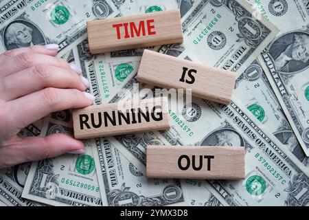 Time is running out symbol. Concept words Time is running out on wooden blocks. Beautiful dollar background. Businessman hand. Business and Time conce Stock Photo