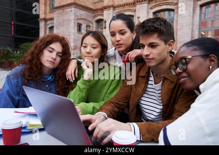 Multiracial students gathered together studying at university campus using a laptop. Stock Photo