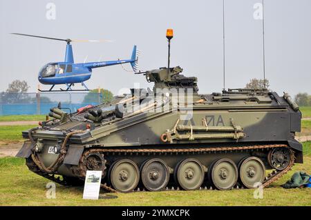 British Army Alvis FV103 Spartan CVRT armoured vehicle on display, with Robinson R44 helicopter flying. Southend Airport event Stock Photo