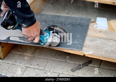 Man using battery powered angle grinder to cut ceramic floor tile Stock Photo
