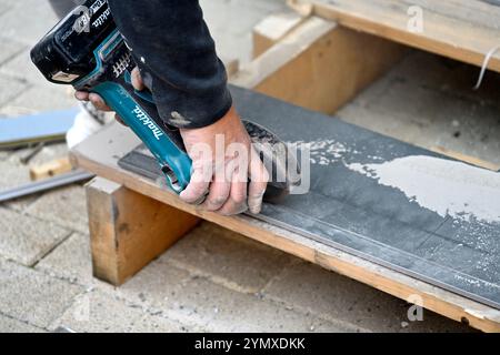 Man using Maktta battery powered angle grinder to cut ceramic floor tile Stock Photo
