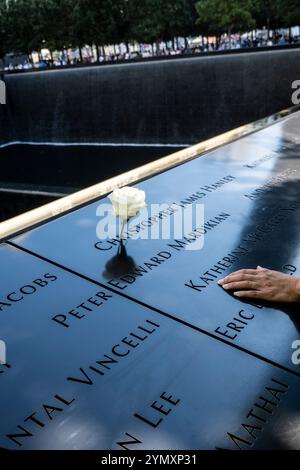 White rose and woman's hand on the parapet showing names of the 9/11 victims surrounding the Memorial Pool at National September 11 Memorial, NYC, USA Stock Photo