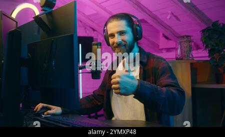 Smiling Caucasian man male blogger cyber sport gamer playing online video game showing thumb up at home satisfied vlogger guy approval gesture success Stock Photo