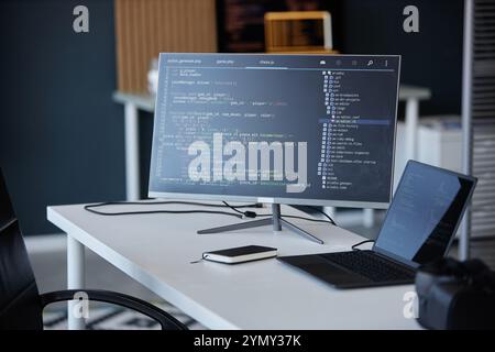 Modern office with a coding interface shown on a monitor, accompanied by a laptop and smartphone, showcasing various technology tools and gadgets in w Stock Photo