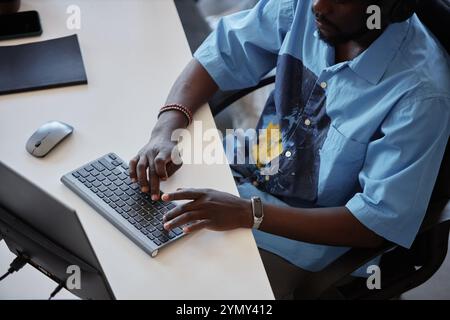Person typing on keyboard in modern office setting, wearing casual attire and surrounded by office tools. Engaging in professional task with focused e Stock Photo