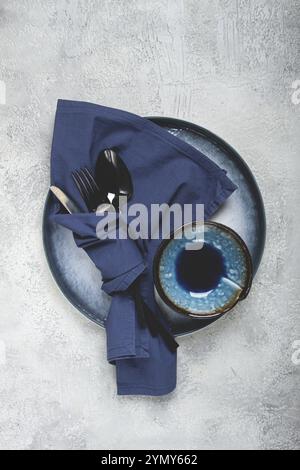 Food background, with an empty blue plate, a bowl, black cutlery, with a napkin, on a gray background, table setting, top view, no people Stock Photo