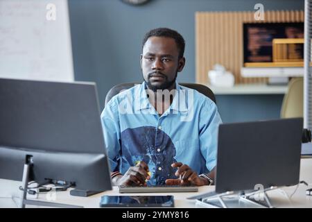 Man sitting at a desk and working with multiple computer screens. Office environment with blurred background showcasing relaxed workspace atmosphere Stock Photo