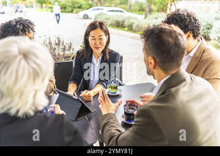 Chinese businesswoman talking with colleagues using tablet and drinking coffee in a cafeteria Stock Photo
