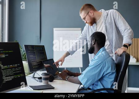 Two colleagues collaborating on software development in modern office space with whiteboard and multiple computer screens during work discussion of pr Stock Photo