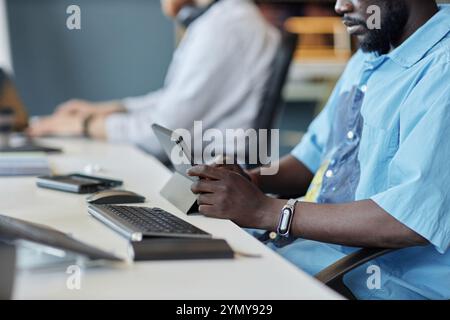 Man sitting at office desk and focused on large tablet while at workplace. Various electronic devices and office supplies spread across the desk in mo Stock Photo