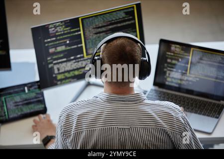 Person seen concentrating on coding projects with multiple screens and advanced technology setup wearing headset. Numerous lines of code visible acros Stock Photo