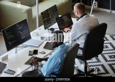 Developers working diligently on software project in modern office. Both focused on coding, surrounded by multiple monitors and tech gadgets, exhibiti Stock Photo