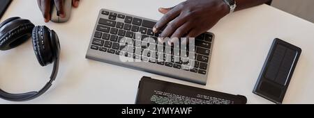 Close-up of hands typing code on wireless keyboard while multitasking with gadgets on clean workspace without visible clutter. Stock Photo