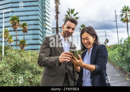 Relaxed and happy multi-ethnic female and male business colleagues using mobile phone at city Stock Photo