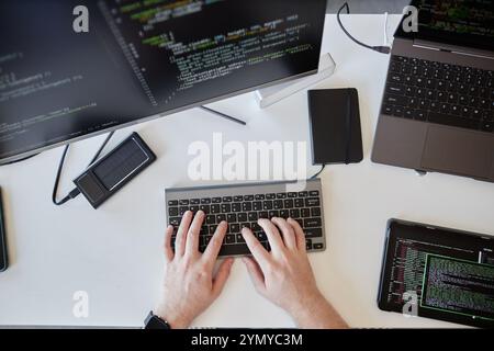 Close-up of hands typing on a keyboard while surrounded by several monitors displaying code and a tablet on desk creating a tech-focused atmosphere Stock Photo