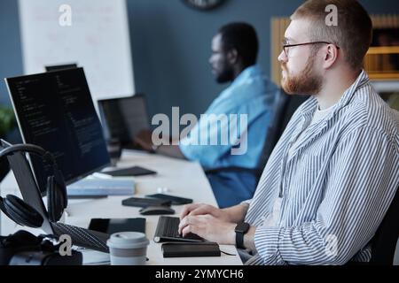 Multi-ethnic group of developers focused on coding and discussing project details in a modern office setting. Senior programmer working on computer sc Stock Photo