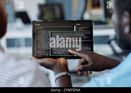 Close-up of two individuals reviewing code displayed on a tablet device with a blurred office background showcasing a collaborative tech workplace mom Stock Photo