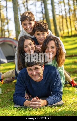 Caucasian family having fun together lying on the forest one on top of each other next to camping tent Stock Photo