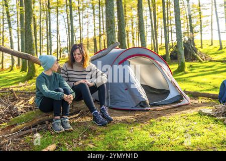 Caucasian happy mother and boy sitting next to camping tent in the forest Stock Photo