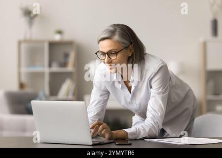 Positive busy grey haired business woman typing on laptop computer Stock Photo