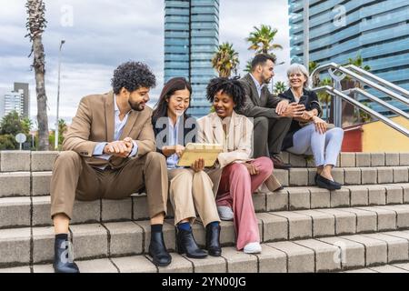 Multi-ethnic and diverse group of business people sitting on outdoor stairs working using digital tablet Stock Photo