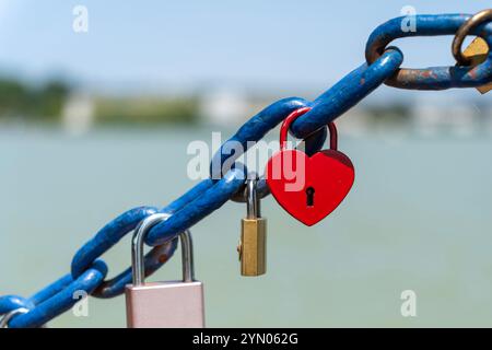Red heart-shaped and other padlocks on a blue chain Stock Photo