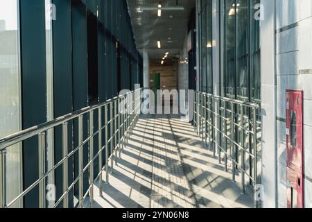 A sunlit corridor in a modern building featuring metal railings and glass walls. The clean architectural design emphasizes linear perspective and brig Stock Photo
