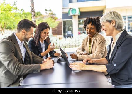 Side view of multi-ethnic happy business people in a meeting using laptop sitting in a cafeteria Stock Photo