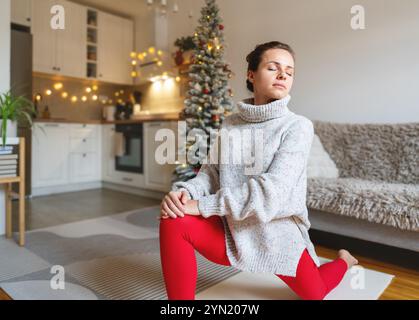 Caucasian female at home practicing yoga stretching exercise during Christmas holidays. Stock Photo