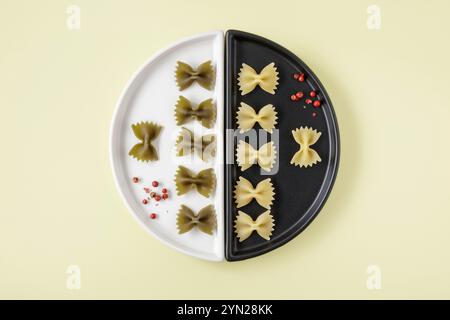 Small Farfalle pasta arranged on black and white plate with red peppercorns Stock Photo