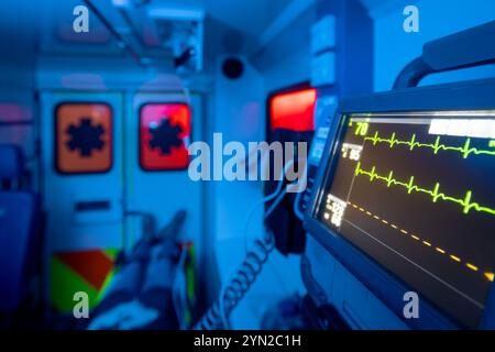 Selective focus on monitor of vital signs against patient on stretcher inside ambulance car of emergency medical service at night. Themes rescue, urge Stock Photo