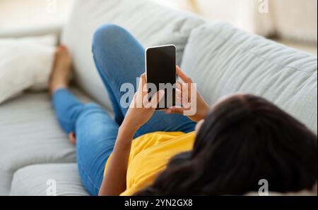 Unrecognizable black woman using cellphone on comfy sofa at home, mockup for mobile app design on screen Stock Photo