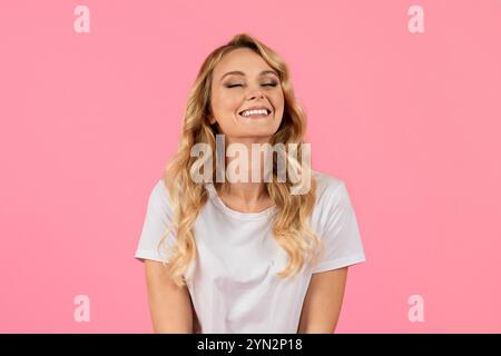 Smiling woman with wavy hair in white shirt against a pink background Stock Photo