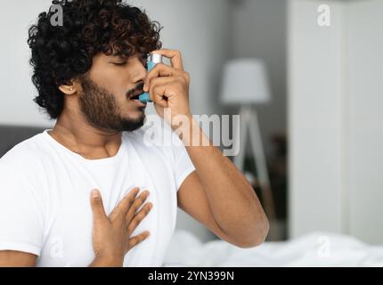 Indian guy suffering from asthma, using inhaler in bed Stock Photo